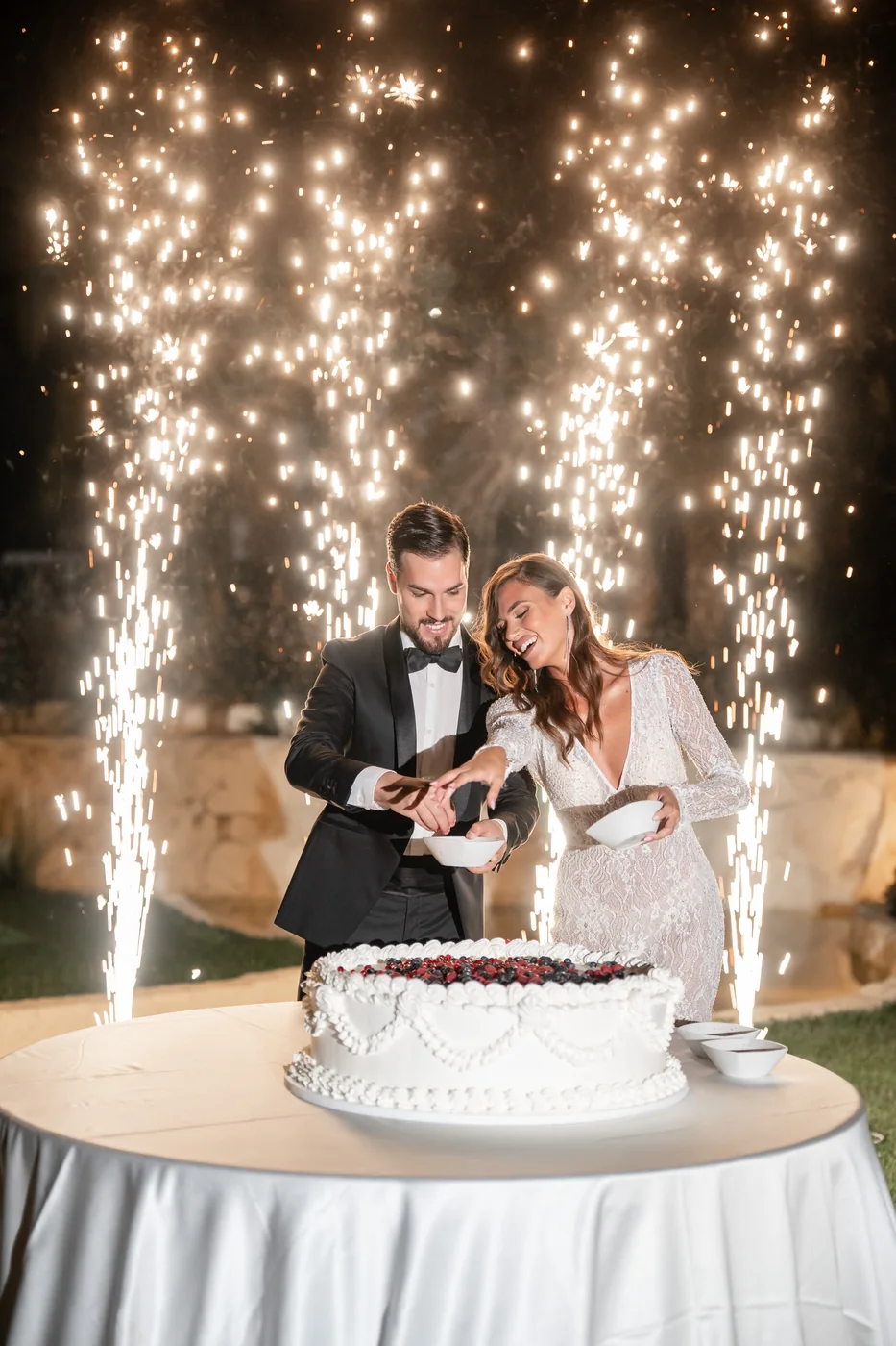 Wedding couple celebrating beside a cake and sparklers, photograph by Mauro Silvestre