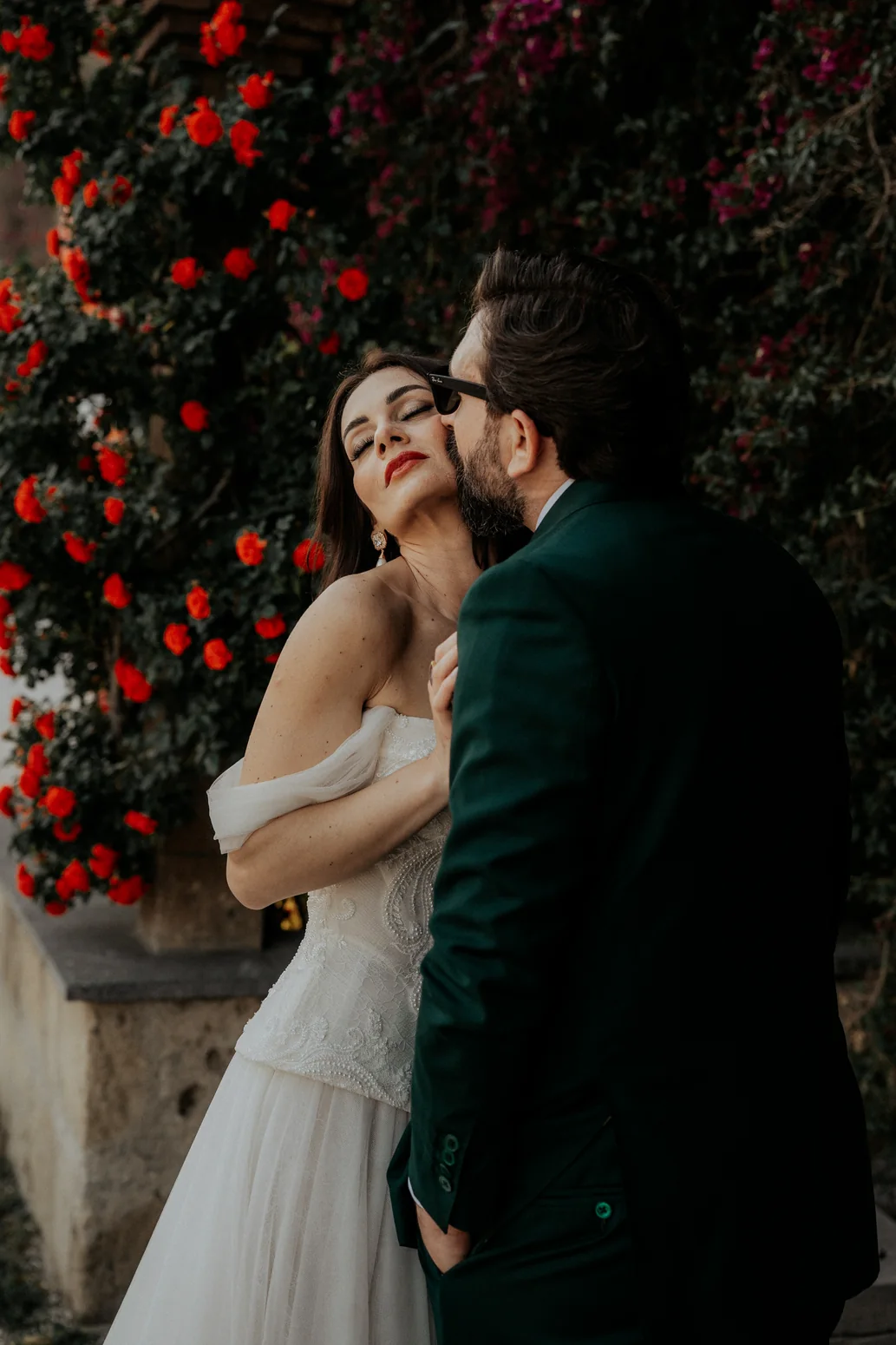 Newlyweds embracing by red flowers, photography by Mauro Silvestre